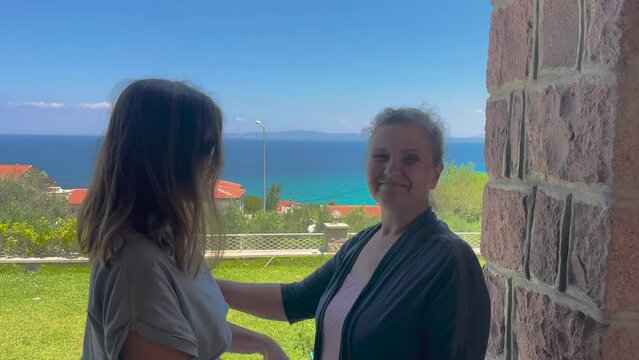 Senior old woman and her daughter is loving theirselves. Hugging, kissing, family concept in summertime, vacation. Sea and grass landscape, happy family.