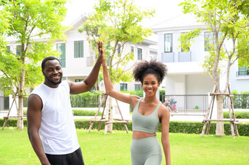 Young African American fitness couple clapping hands together while standing in the park after successful outdoor training. Fitness partners give a high five. healthy concept.