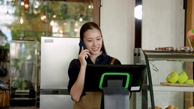 Beautiful Asian woman owning a small business. open coffee shop Taking orders from customers who ordered food by phone Preparing coffee. stand behind counter preparing drinks in cafe.