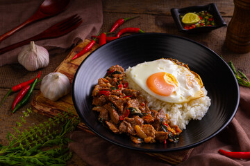 Stir fried sliced Beef with Holy Basil and Cooked Rice topped with fried egg in black plate.Thai spicy food(Pad Kra pao) - obrazy, fototapety, plakaty