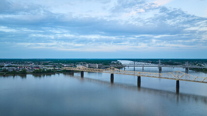 Obraz premium Suspension truss bridges over blue river under deep blue sky leading to distant green shore aerial
