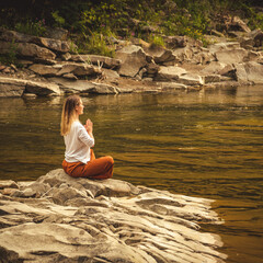 Woman doing yoga on the stone at the mountain river. Carpathians
