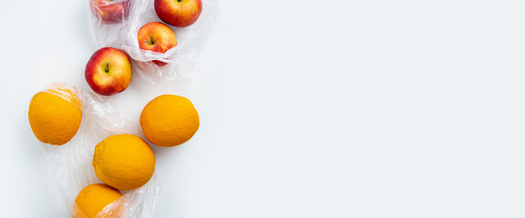Fresh ripe oranges, apples in transparent bags on a white background. Top view, flat lay. Banner