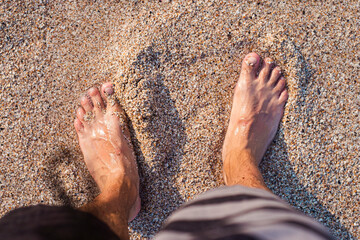 Men's bare feet stand on the sandy beach. Top view, flat lay - obrazy, fototapety, plakaty