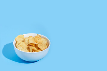 Potato chips in a bowl ready to eat on a blue background.