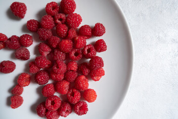 Fresh, ripe raspberries in a light plate on a light background. Photo from above. The concept of proper nutrition, diet