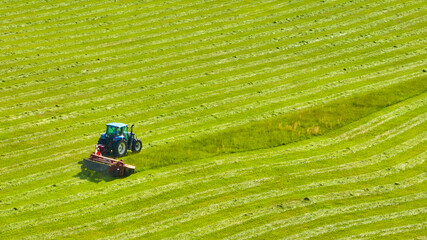 Aerial tractor mowing grass field with neat rows of owed grasses background asset