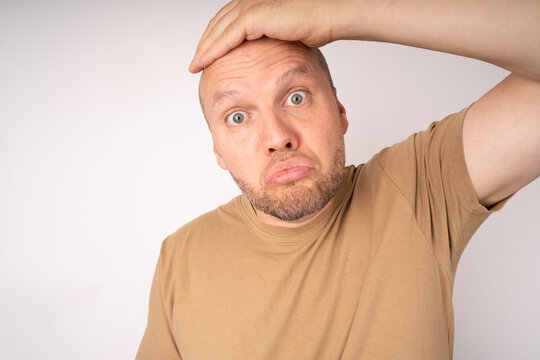 Young man holds his hand to his forehead, puffs out his eyes and lips and make a questionable gesture