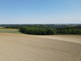 Obraz premium Drone view of brown plowed arable fields with dirt, trees and a blue sunny sky in summer