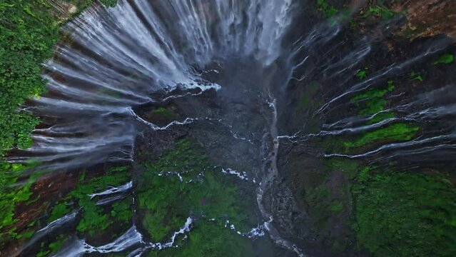 Aerial top view drone rise up and spin from bottom of Tumpak Sewu waterfall, multiple falls flow into steep canyon, Malang, East Java, Indonesia
