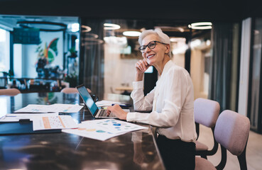 Thoughtful senior businesswoman sitting at table looking away at work