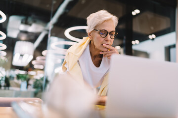 Thoughtful senior woman sitting with laptop in cafe