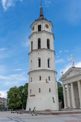 Vilnius Cathedral, with people walking through the square, on a day with a blue sky and some clouds.