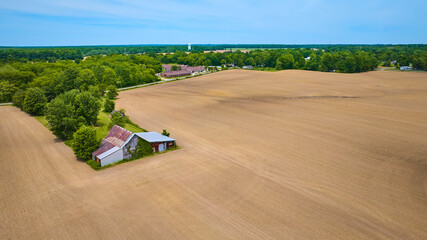 High up aerial view of empty dirt farmland with brown scar on land and old barn