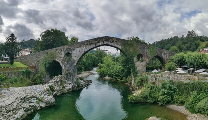Fototapeta na wymiar Panoramic view at the Roman bridge over Sella river, an iconic bridge on Cangas de Onís downtown city, Picos de Europa or Peaks of Europe, Cantabrian Mountains, Spain