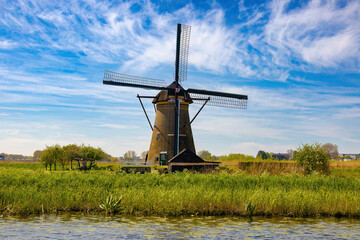 Naklejka premium A large windmill on the other side of the channel stands like a great giant in the middle of the vast plain. Kinderdijk, The Netherlands.