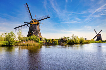 View from the canal, the shore showing two windmills and one in the background in perspective....