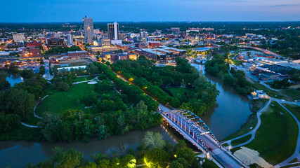 Wide view aerial downtown Fort Wayne at dusk with lights on bridge and buildings