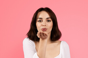 Happy millennial caucasian brunette woman making blowing kiss with hand