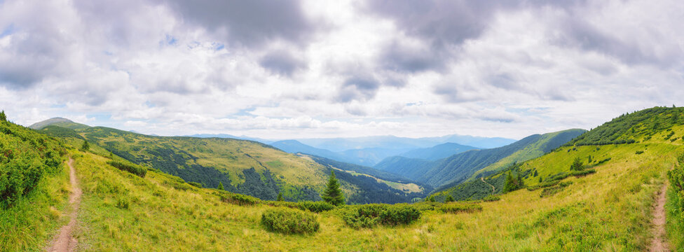 hiking through ukrainian highlands with grassy alpine meadows in summer. panoramic view in to the distant chornohora ridge and green forested valley. cloudy weather with overcast sky