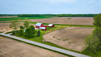 Property farm farmhouse barn and shed green pasture empty plowed fields with paved road aerial