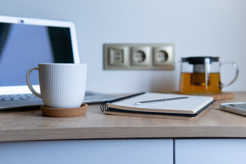 working atmosphere a cup of coffee on the background of a laptop and a notepad on a wooden table close-up with a blurred background