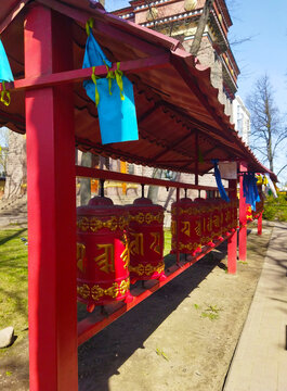 Red prayer wheels near Buddhist temple - The Datsan Gunzechoinei in Saint Petersburg. Close-up view of traditional religion symbols, prayful subject of buddism. St. Petersburg, Russia. May 09, 2023