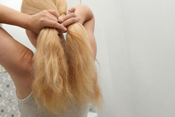 Blonde woman braiding her hair, close up photo. Hair Braid. Rear view closeup. Woman tied her in braid at home