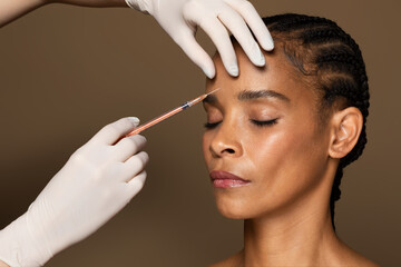 Beautician hands making hyaluronic acid injection, black middle aged woman getting cosmetic...