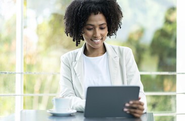 Cheerful young black lady entrepreneur sitting at cafe, using tablet