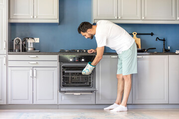 Young positive man cooking food in the oven