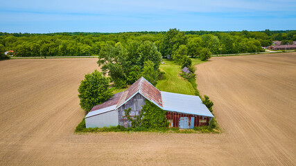 Old rusty barn in center with empty dirt farmland on three sides and a lush green forest behind...