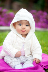 Sweet six months old baby girl sitting at the garden in a beautiful sunny day