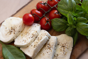 Fresh mozzarella, tomatoes, and sweet Italian basil on a wood cutting board next to a kitchen window at sunset 