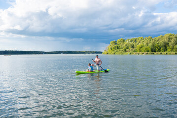father and son ride a SUP board, father and child spend time outdoors on the lake