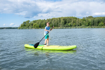 Fototapeta na wymiar A 10-year-old boy rides a SUP board on a river or lake alone