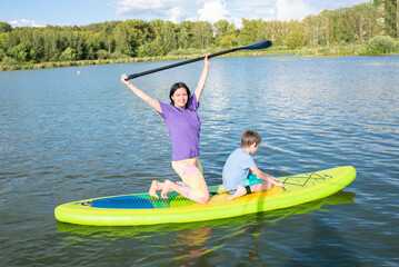 a woman with her son rides on a stand-up board on a sunny day in summer.. A mother with a child on a SUP board spends the weekend on the lake, in nature