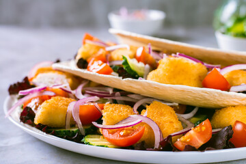 Close up of tacos with chicken nuggets, cucumber, tomato, onion and lettuce on a plate