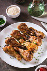 Appetizing baked chicken legs with chives and sesame seeds on a plate vertical view