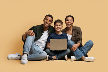 Positive happy african american family using laptop on beige