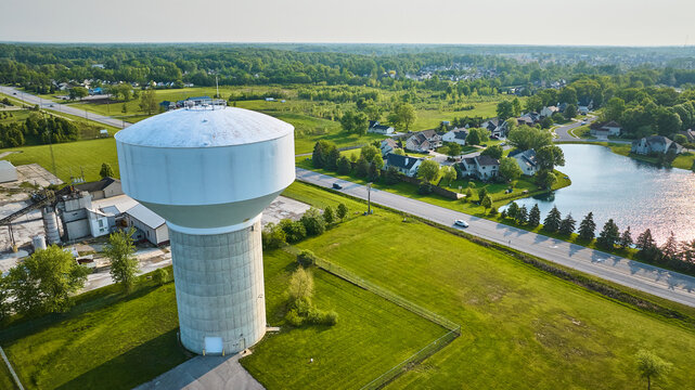 Water tower near processing plant and neighborhood in rural area with pond aerial