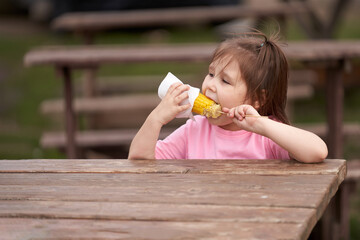 A child biting a corn cob at a wooden table at a summer equipped camp for campers.