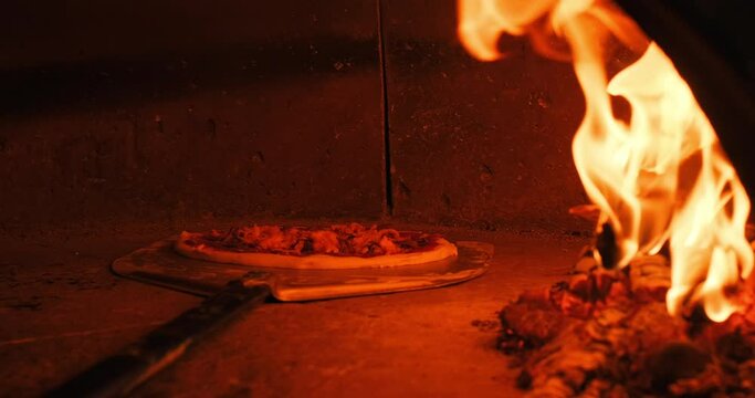 Closeup shot of placing pizza in wood fired pizza oven using a pizza peel. Traditional italian pizzeria