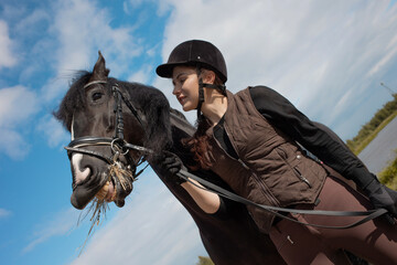 Equestrian sports. A young woman, a rider and her horse, portrait against a clear sky