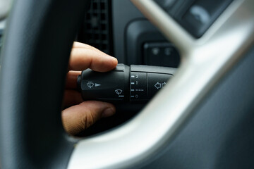 A man's hand turns on the windshield wiper switch control lever in a truck