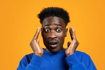 Shocked millennial african guy looking aside, yellow background