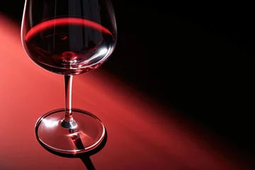 Fotobehang Red wine in a glass on dark red and black background. Wineglasses. Romantic drink for party, wine shop or wine tasting concept. Hard light. Copy space © ratatosk