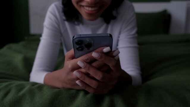 Modern technoligies concept with happy smiling afrocan gorl in headphone with phone lying on bed.Social media,dating app