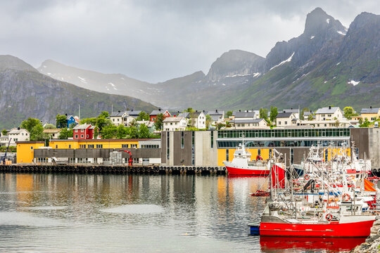 Fishing boats at the pier with village houses and mountain in the background at Husoy village, Senja island, Norway