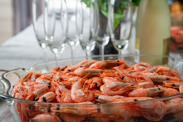 A dish of unpeeled shrimp on a dinner table with plates. Seafood diner. Boiled shrimps. vegetarian dinner, food.